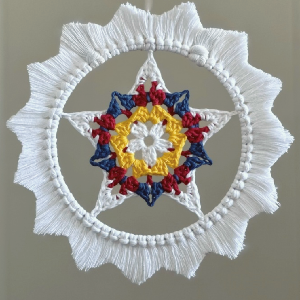 A crocheted parol - a star inside a hoop with a macrame sunburst border. The star is white, yellow, red, and blue, like the colors on the flag of the Philippines. The fringe border is white.
