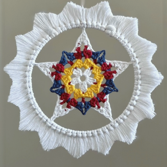 A crocheted parol - a star inside a hoop with a macrame sunburst border. The star is white, yellow, red, and blue, like the colors on the flag of the Philippines. The fringe border is white.